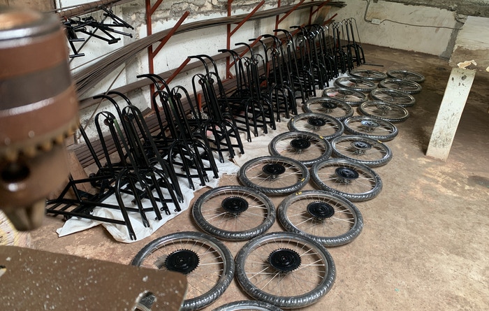 A large batch of wheelchair frames sit on the workshop floor waiting to be assembled. In front of them lay all the wheels and components which will be used to turn these into SafariSeat wheelchairs. 
